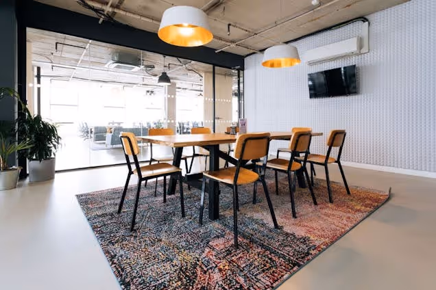 A meeting room featuring a wooden table with black chairs on a rug under pendant lights.