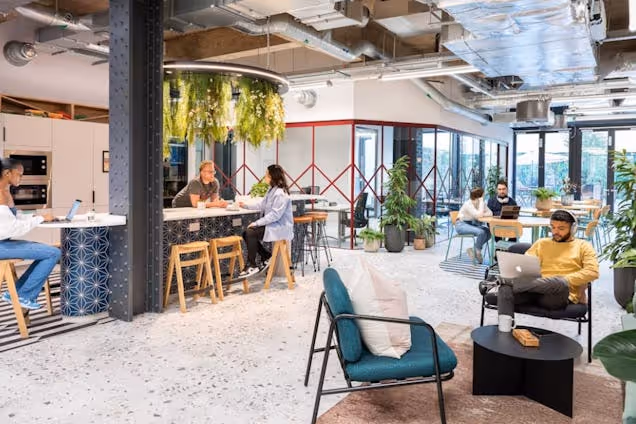 People sat on chairs and people working at a kitchen island with hanging plants in an office breakout area.