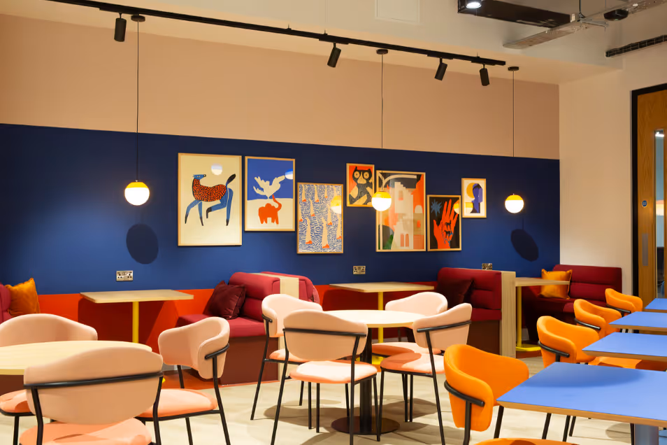 Runway East Birmingham breakout area featuring tables and cream, red, and orange chairs