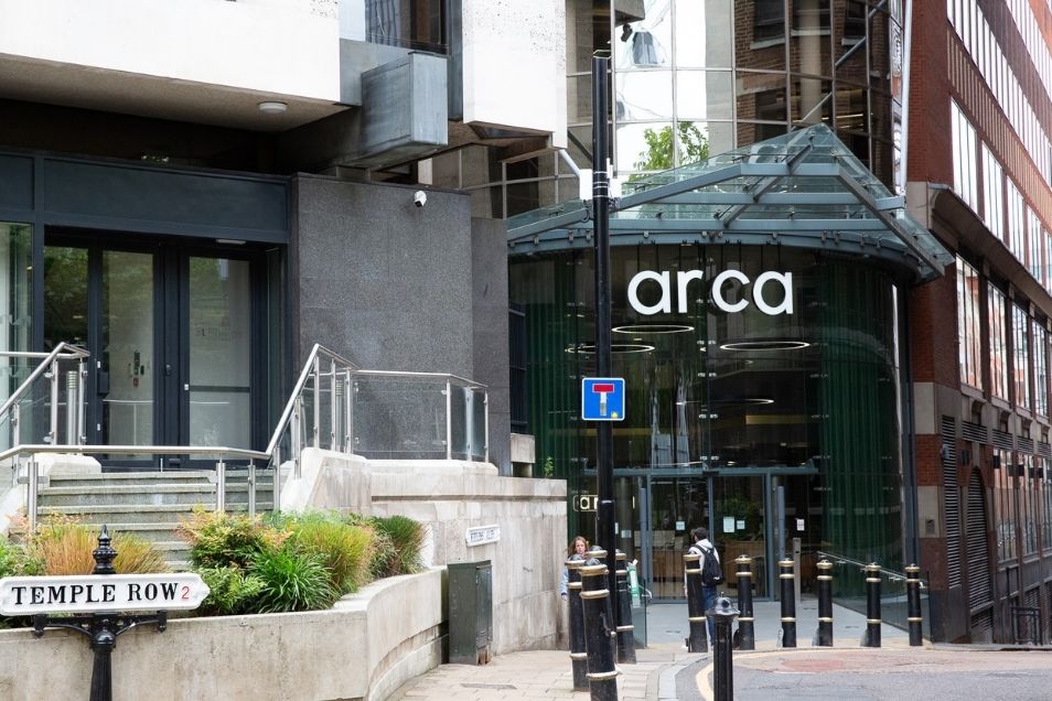 Entrance to the "arca" building, featuring a curved glass storefront and a "TEMPLE ROW" street sign in the foreground.