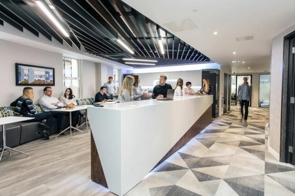 Busy office reception featuring a sleek white angular desk and people collaborating in a bright, geometric-tiled lounge.