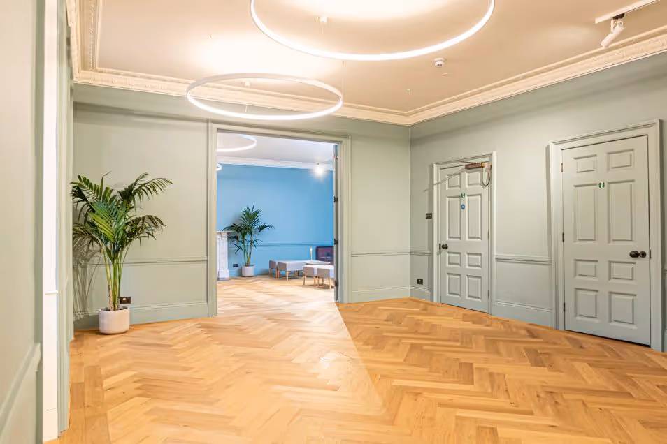 A bright office foyer with sage green walls, elegant parquet flooring, and circular LED pendant lights.