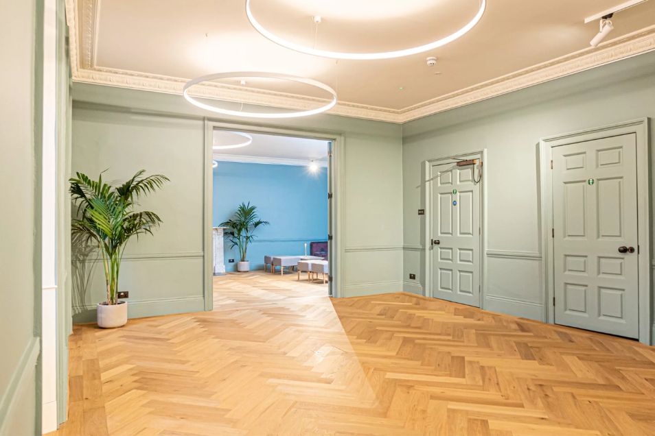 A bright office foyer with sage green walls, elegant parquet flooring, and circular LED pendant lights.