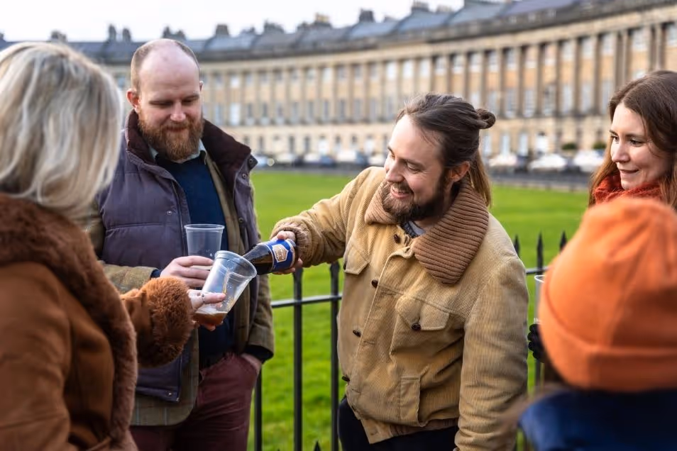 A man pours a drink from a bottle into a plastic cup for a group of people outdoors.