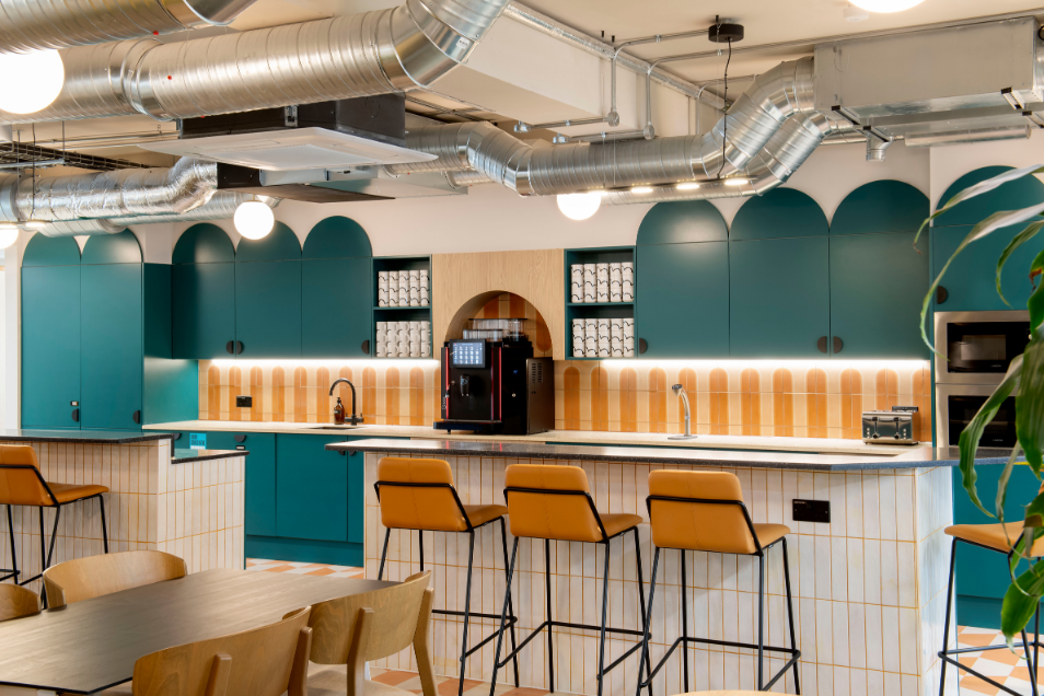 Stools sit at a counter in an office kitchen with teal cabinets and a coffee machine.