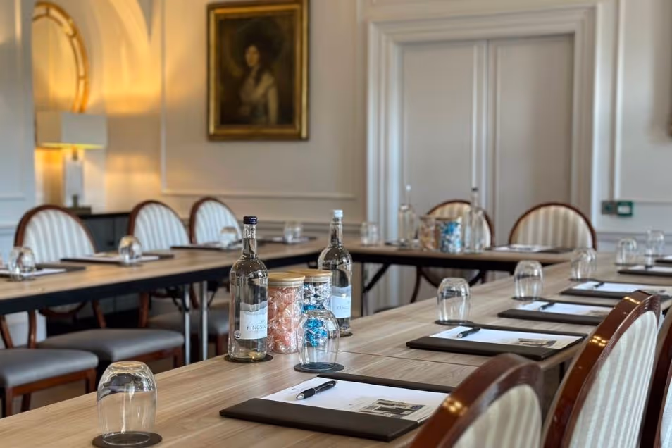 Formal meeting room with a U-shaped table setup featuring water carafes, glasses, and notepads in a traditional panelled interior.