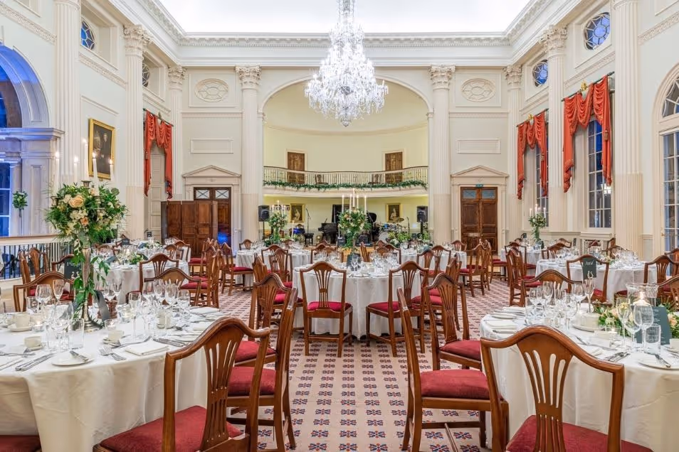 A ballroom set for a banquet with round tables, white linens, floral centrepieces, and a grand crystal chandelier.