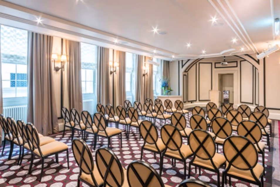 A presentation room with patterned carpet and rows of chairs featuring decorative circular-patterned backs.