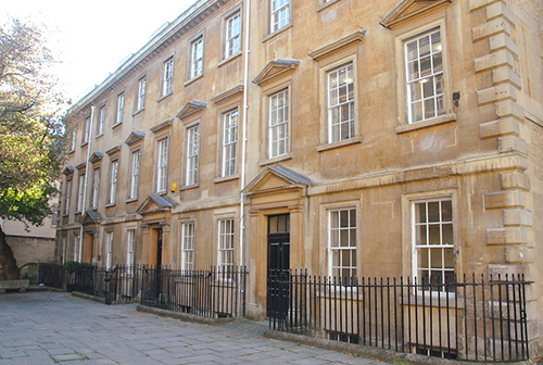Historic tan stone building with white-framed sash windows and a black iron fence