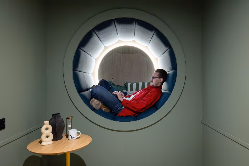 A person in a red jacket relaxes in a circular wall seating nook illuminated by soft lighting.