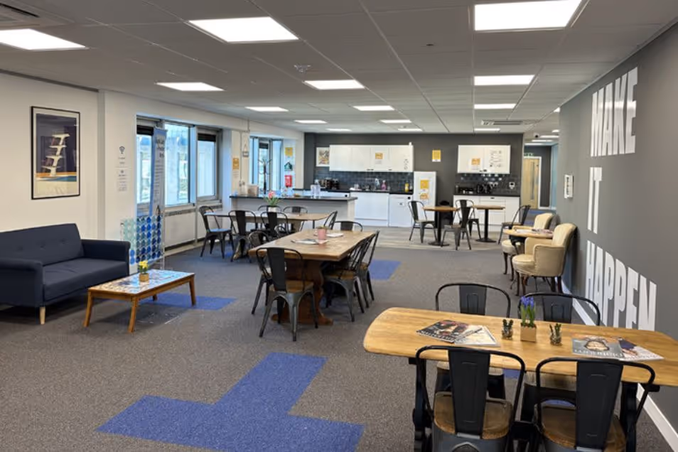 A coworking space with wooden tables and black chairs next to a lounge area and kitchen.