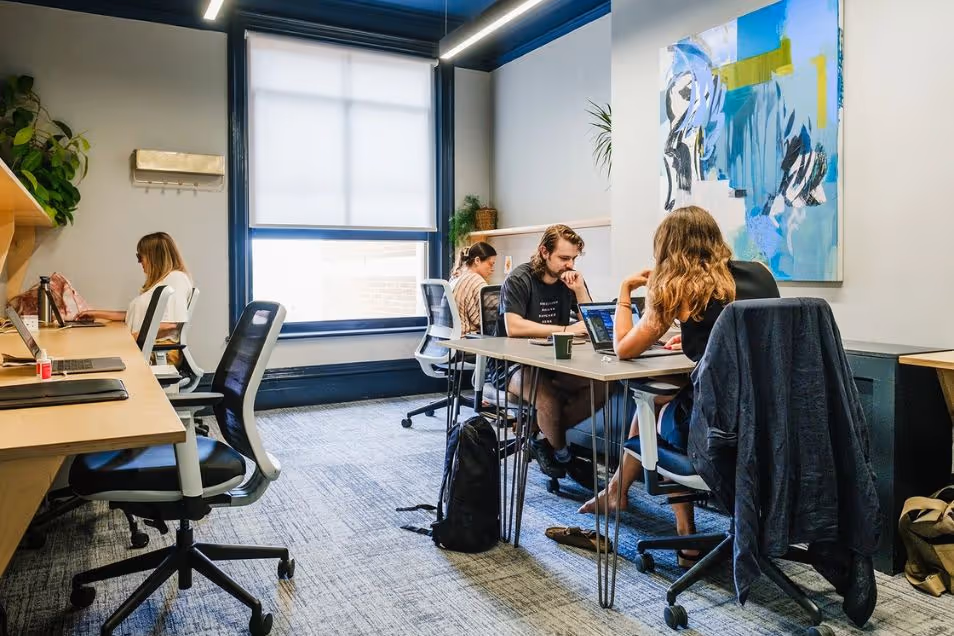 People sitting at a desk and a table working in a coworking space with a mural and a window.