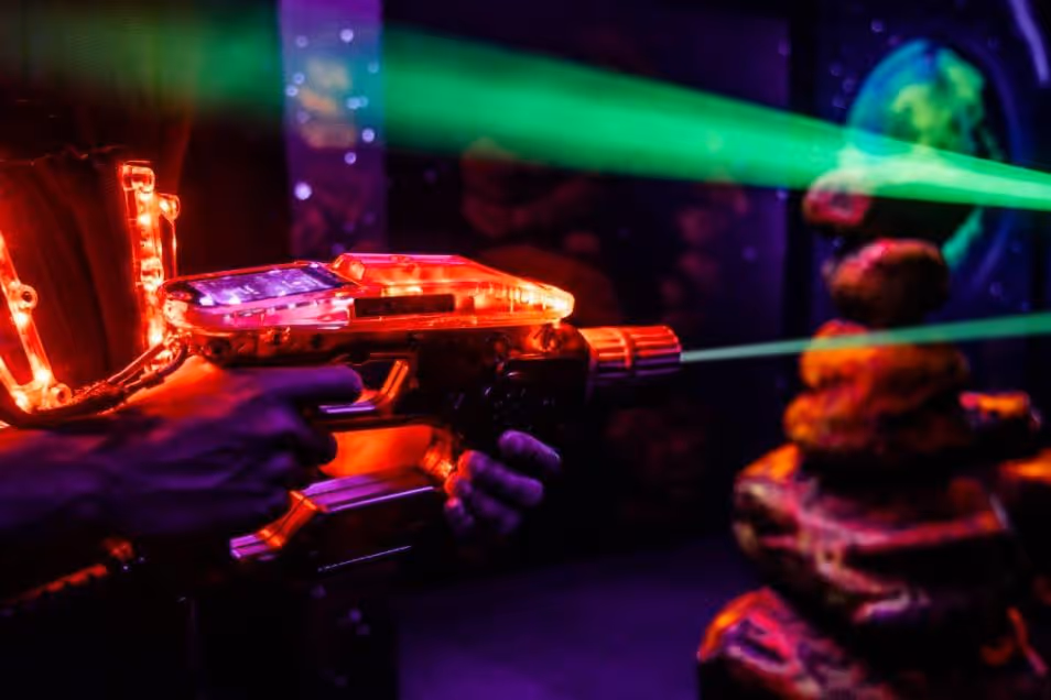 A hand holds a laser tag gun that emits a beam of light in a dark room.