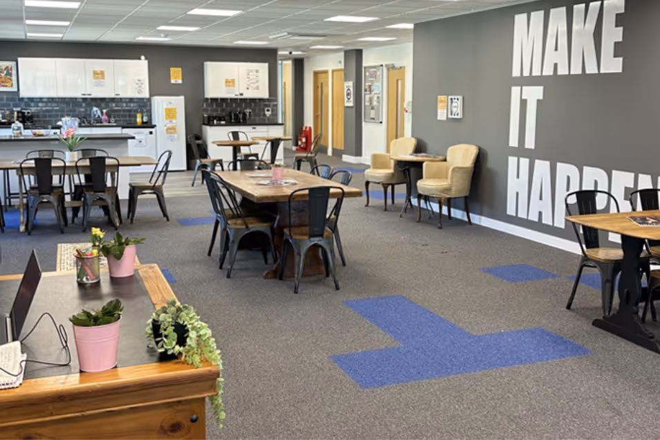 A communal office kitchen and breakroom with dining tables and a wall featuring the text "MAKE IT HAPPEN."