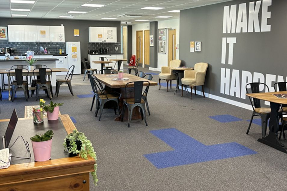 A communal office kitchen and breakroom with dining tables and a wall featuring the text "MAKE IT HAPPEN."