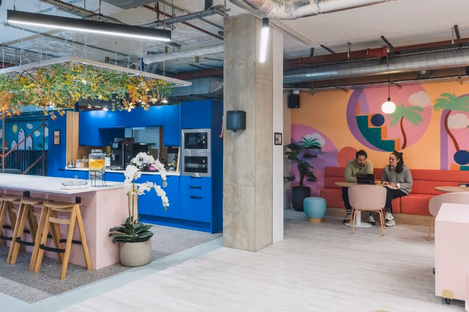Two people sit and work at a small table in a vibrant kitchen area with blue cabinetry.
