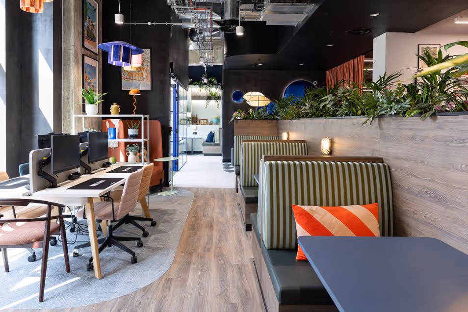 An office featuring striped privacy booths with orange pillows alongside a row of white computer workstations.