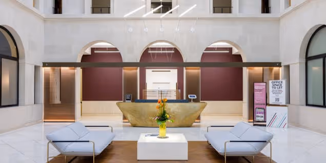 Two grey sofas sit in a building reception in front of a gold reception desk and arched doorways.