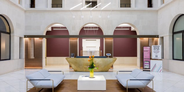 Two grey sofas sit in a building reception in front of a gold reception desk and arched doorways.