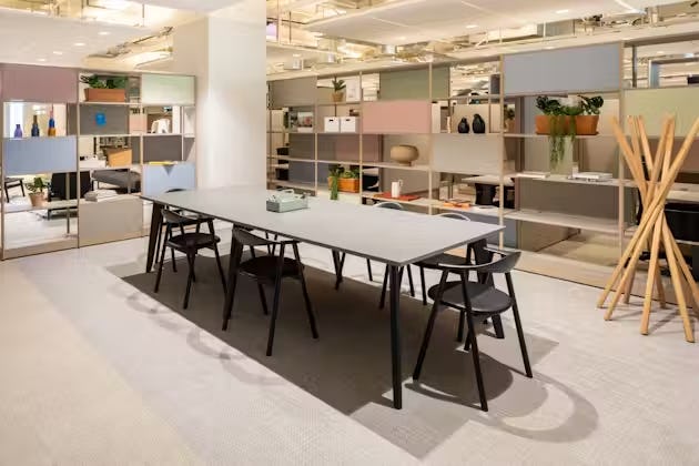 A grey table with black chairs sits in an office near a wall of shelves and a wooden coat rack.