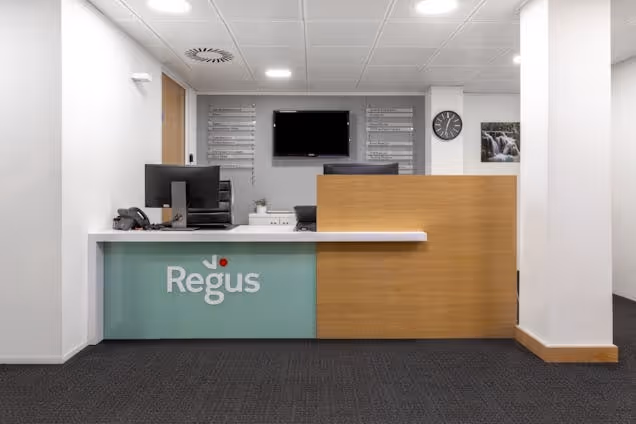 A reception desk with a Regus logo and a computer monitor in an office reception area with white walls.