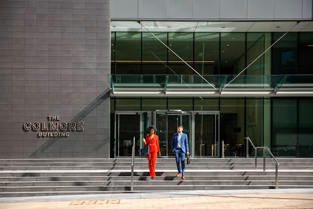 Two people in suits walking down the stone stairs in front of the glass entrance to the Colmore Building.