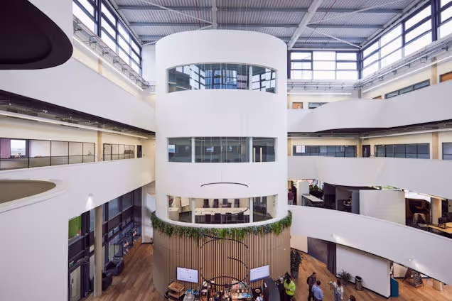 An atrium inside a building with multiple floors, white balconies, and people at tables on the ground floor.