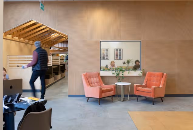 An image of a breakout space with two pink arm chairs and a window into a meeting room.