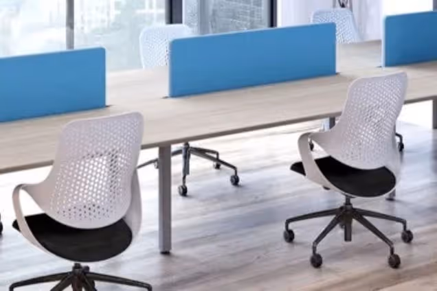 White and black chairs sit at a wooden desk with blue privacy screens on a wooden floor.