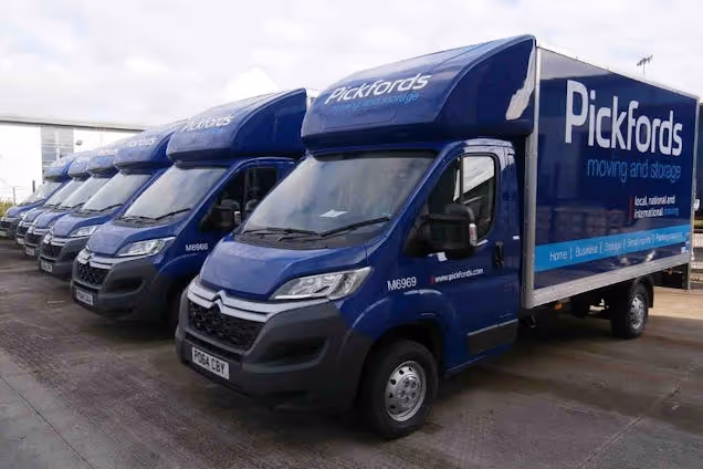 A row of blue Pickfords moving and storage vans parked side-by-side in a parking lot.