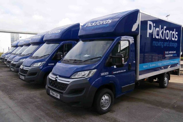 A row of blue Pickfords moving and storage vans parked side-by-side in a parking lot.