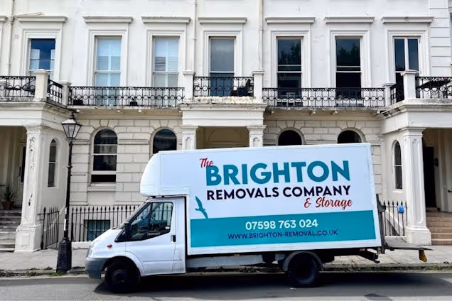 A white Brighton Removals Company & Storage van parked in front of a stone terrace building with balconies.
