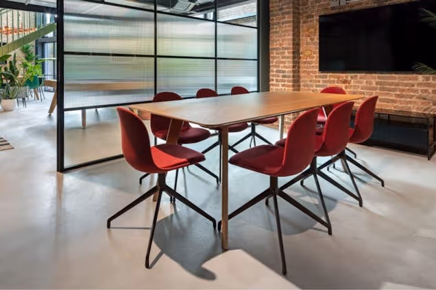 Red chairs surround a wooden table in a room with a brick wall and a television.