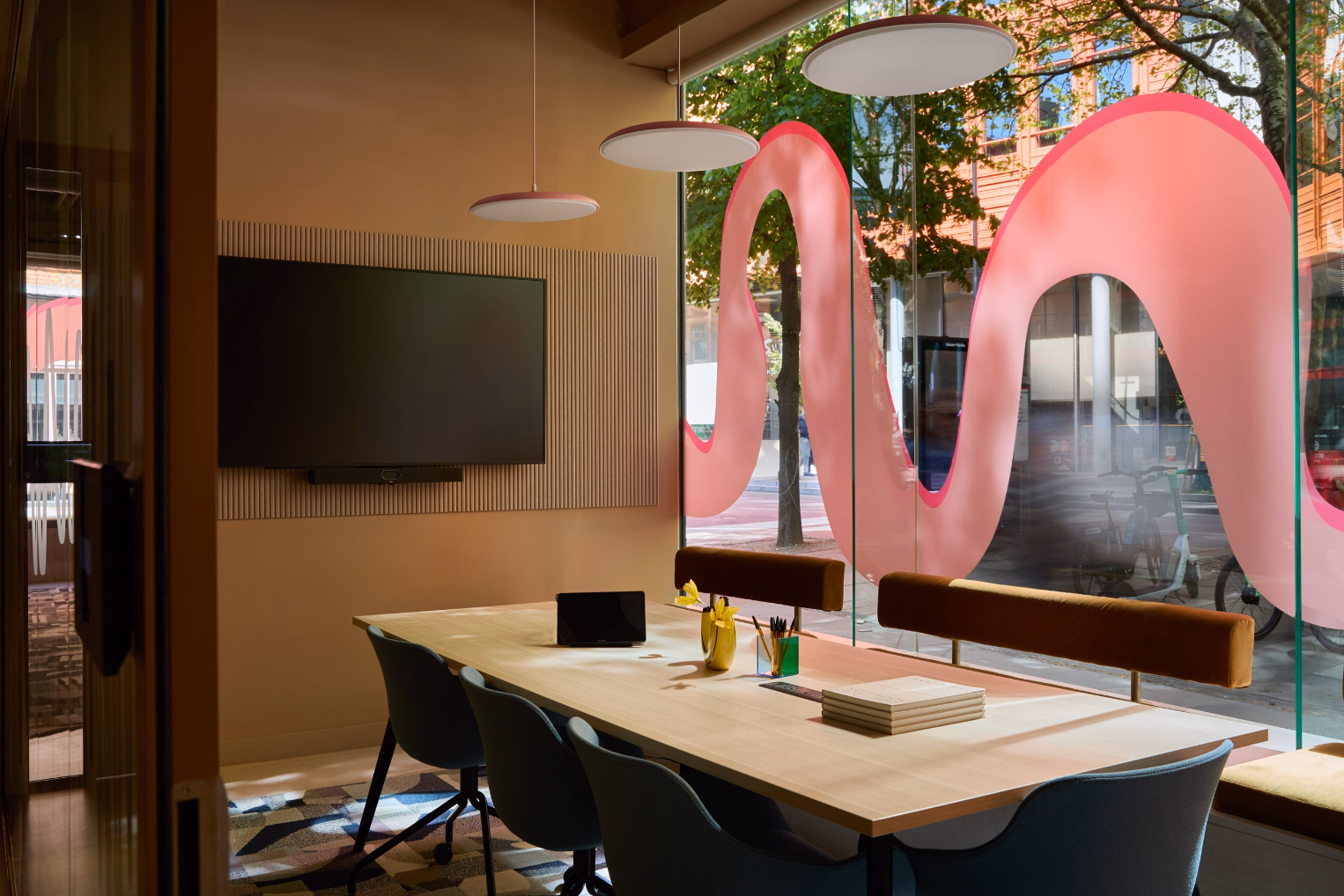 Blue chairs and brown benches sit at a wood table on a rug. A black TV hangs on a wall near white lights and a window with a pink graphic.