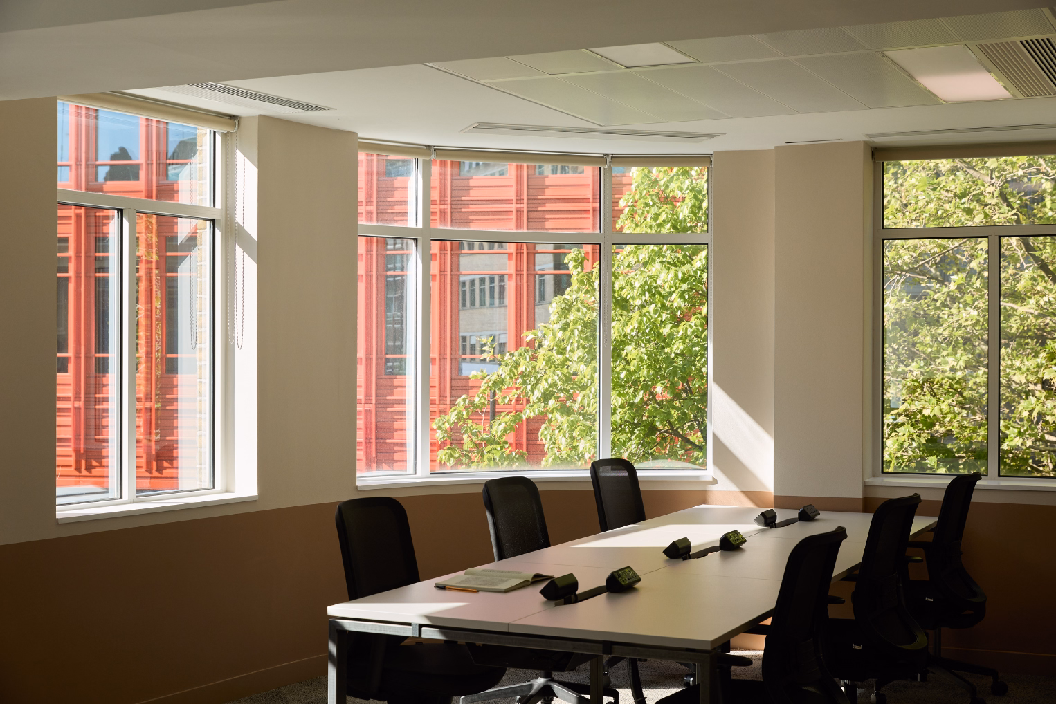 Black chairs sit at a white table near windows showing a red building and trees.