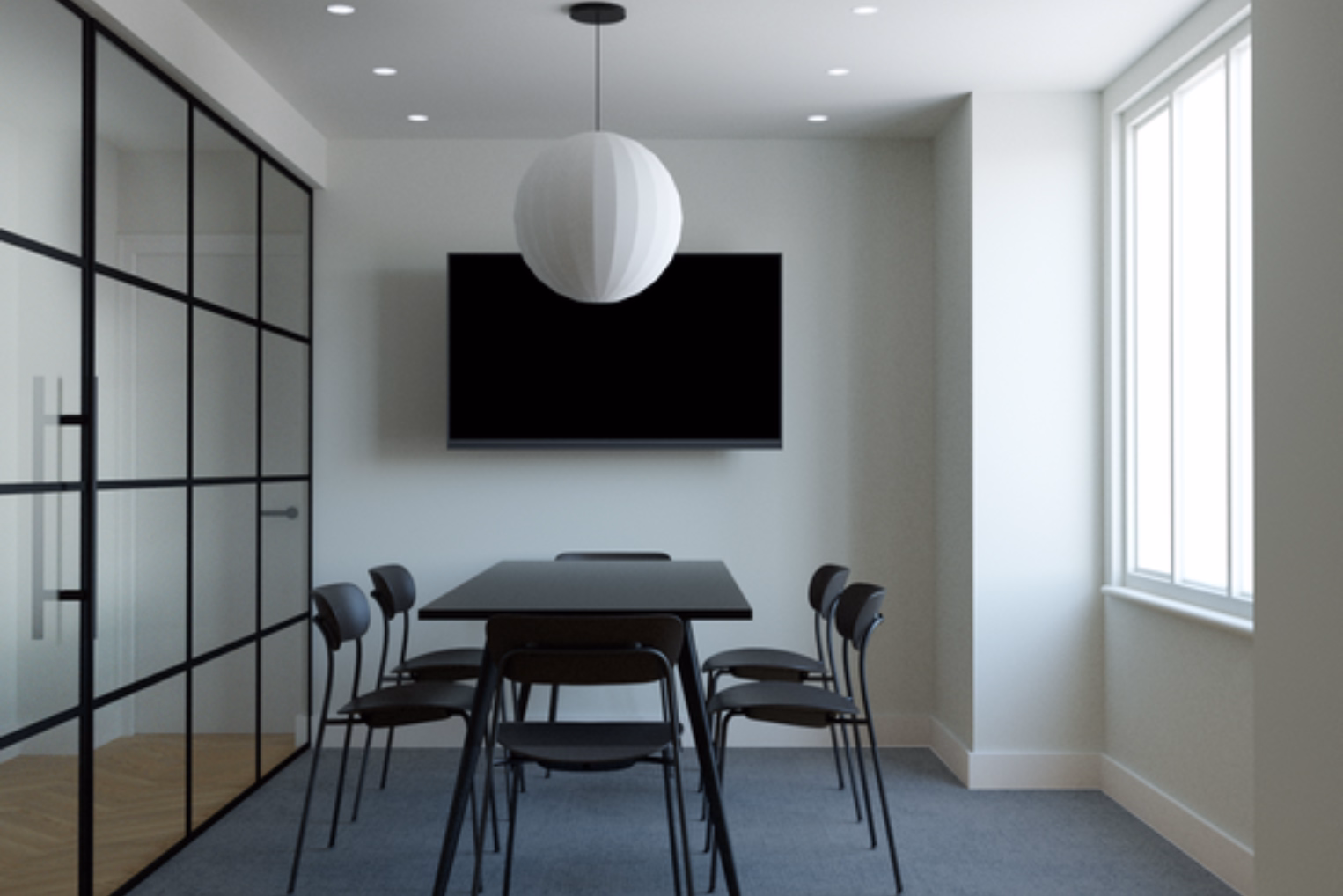 Black chairs at a black table on a grey floor. A white round light hangs near a black TV and a glass wall with black frames.