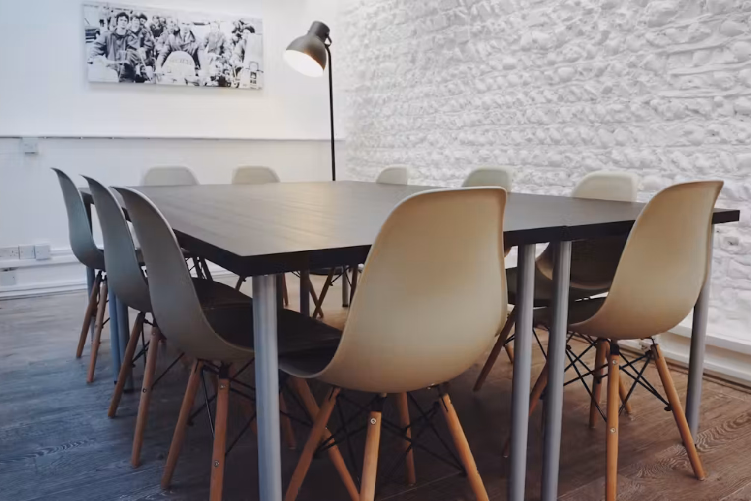 Grey chairs at a black table on a wood floor. A black lamp is near a white wall with a picture.