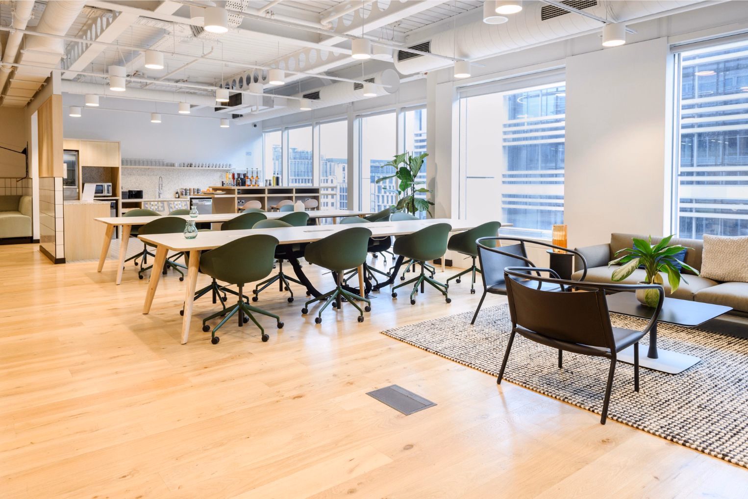 Green chairs at white tables on a wood floor. Black chairs and a grey sofa on a rug near windows under white lights.