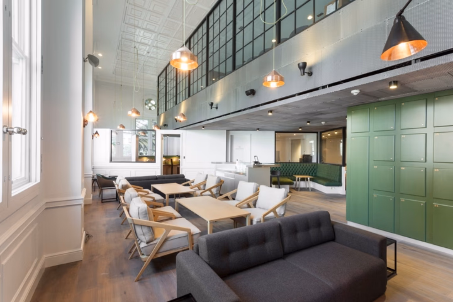 Grey sofas and wooden chairs at wooden tables on a wood floor near green lockers under lights.