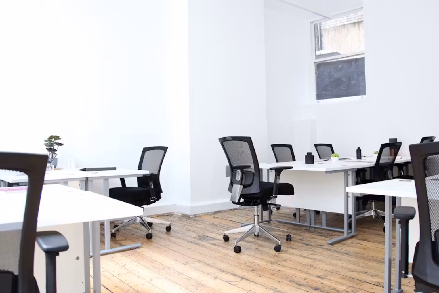 Black chairs sit at white desks on a wood floor near a window.