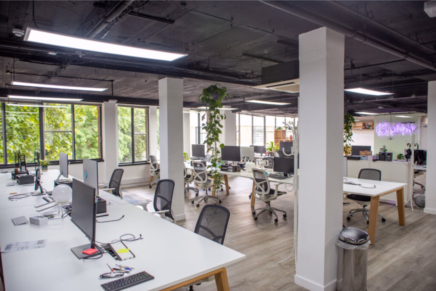 Black and white chairs at white desks on a wood floor near columns and windows under ceiling lights.