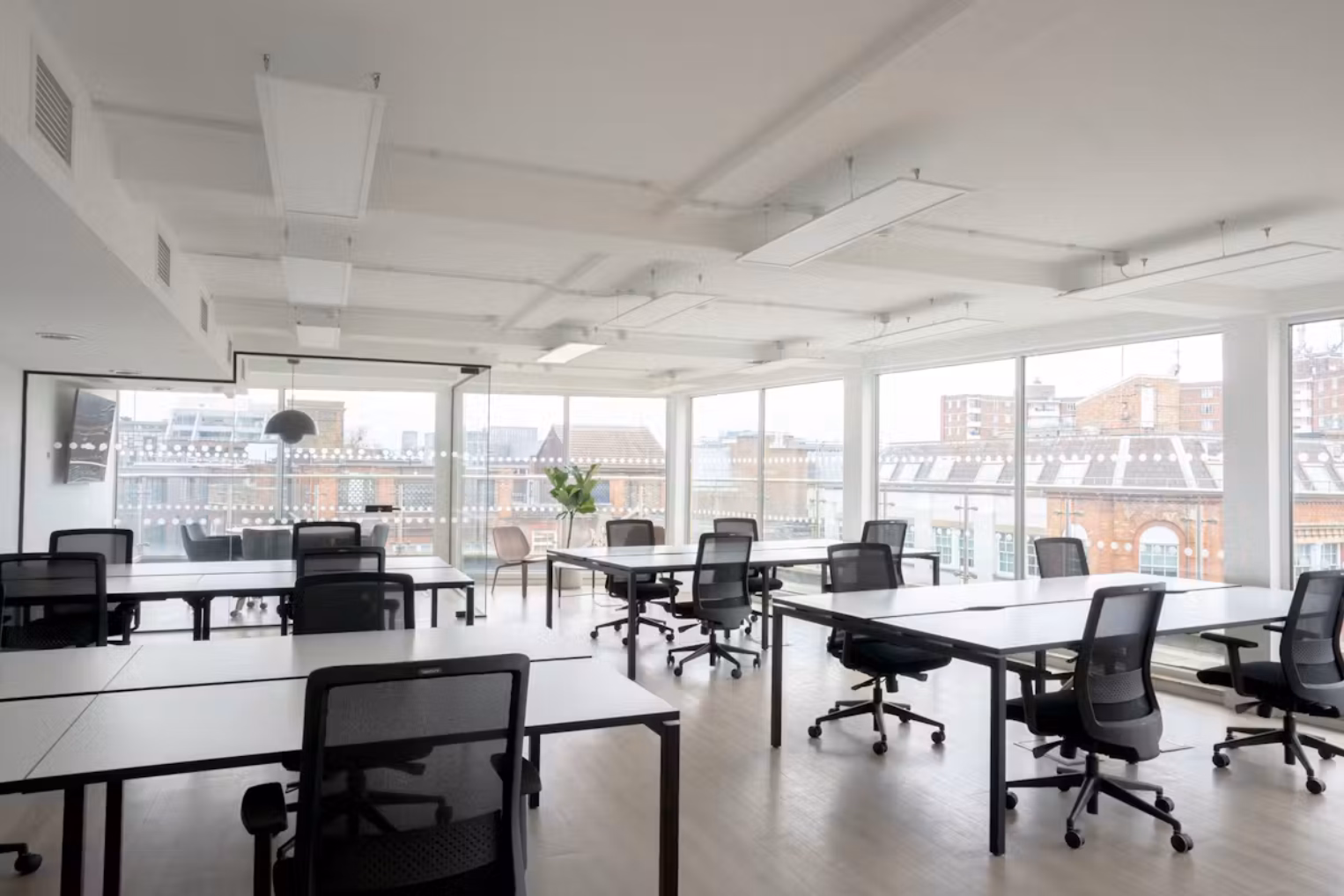 Black chairs at white desks in a room with full glass windows. A glass-enclosed meeting room with grey armchairs.