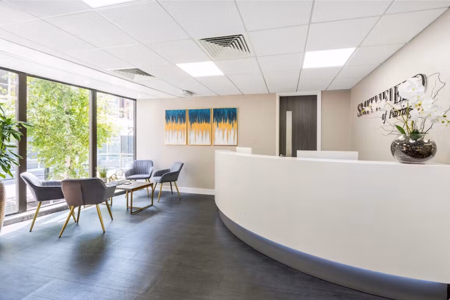 A reception area with a white counter next to a seating area with grey armchairs and a table.