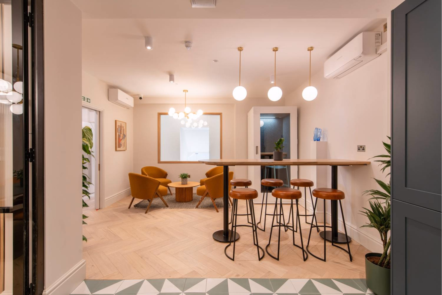 A wooden counter with brown leather stools stands near yellow armchairs and a small wooden coffee table.