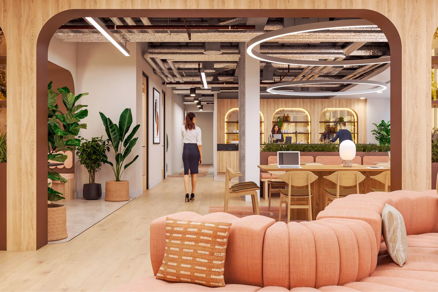 People walking around a brown wooden table with tan wooden chairs near a pink sofa.