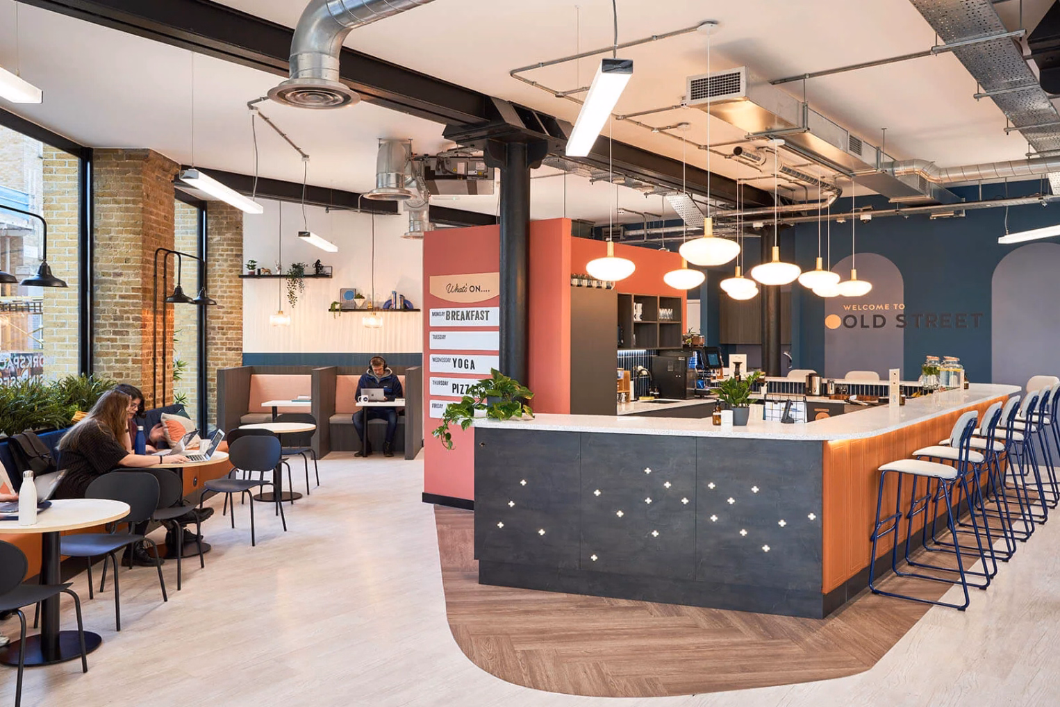 A kitchen counter with high stools in a communal space featuring a "Welcome to Old Street" sign and individual seating booths