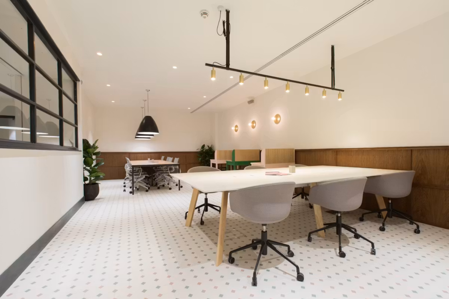 Light grey office chairs sit around long white work tables on a white tiled floor with multi-coloured diamond accents, set against white walls.