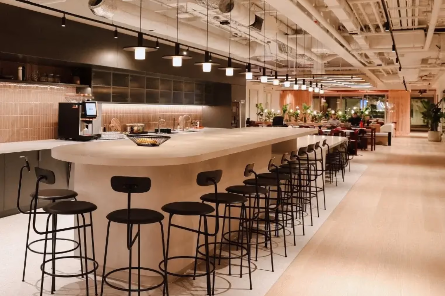 Black barstools line a long, rounded beige kitchen island under a row of black pendant lights.