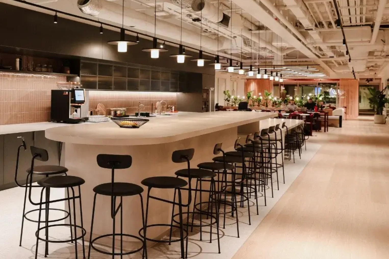 Black barstools line a long, rounded beige kitchen island under a row of black pendant lights.