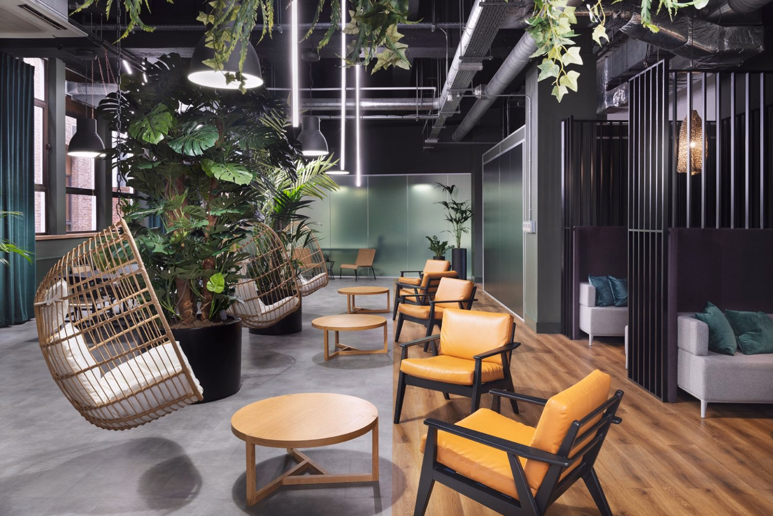 Tan leather armchairs with black frames are paired with low wooden coffee tables, opposite hanging wicker egg chairs among green potted plants.